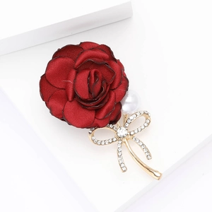 Elegant dark red fabric rose brooch with white pearl and rhinestone bow on a pedestal