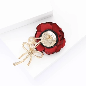 Detail of red fabric rose brooch with golden bow, white pearl, and metal safety pin