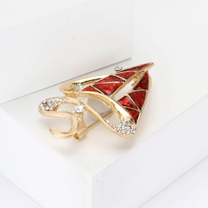 Elegant gold sailboat brooch with red enamel and sparkling crystals on a white pedestal