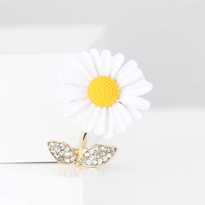 Vue macro de la broche marguerite aux pétales blancs et feuilles dorées en strass