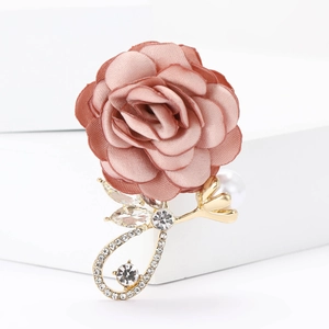 Vue détaillée d'une broche rose en tissu poudré avec cristaux et perle sur socle doré