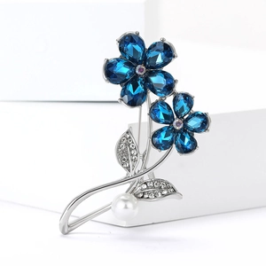 Détail d'une broche fleur avec pétales en cristal bleu, feuilles et perle blanche