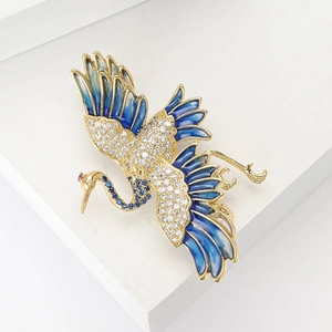 Exquisite golden crane brooch with blue cubic zirconia and enamel on a white stand