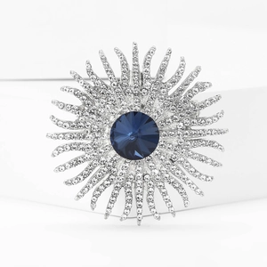 Macro shot of silver sunburst brooch with large blue gemstone and white rhinestones
