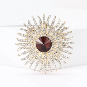 Elegant gold sunburst brooch with a large ruby red gemstone and sparkling white rhinestones