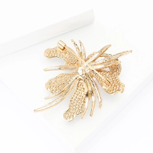 Detailed back view of the orchid brooch showing the pin clasp and golden textured finish