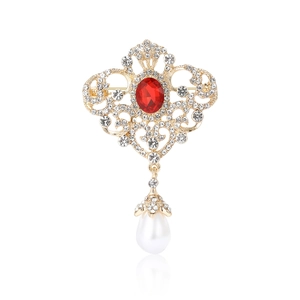 Broche vintage en alliage doré avec gemme rouge et perle pendante sur un fond blanc pur