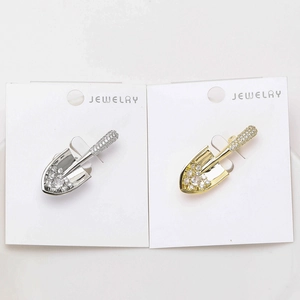 Detail of shovel-shaped brooches in gold and silver finish with sparkling zircon inlay