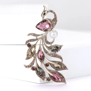Luxury gold peacock brooch with purple crystals and pearl on a white pedestal