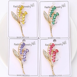 Dettaglio di quattro spille a mughetto colorate con strass e placcatura in oro