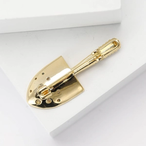 Detailed close-up of a luxury gold shovel brooch with a polished mirror finish on a pedestal