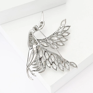 Macro shot of silver crane brooch with marquise-cut crystals on white geometric block