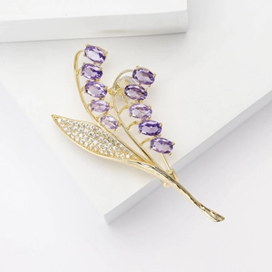 Elegante spilla a mughetto con zirconi viola e foglia oro su piedistallo bianco