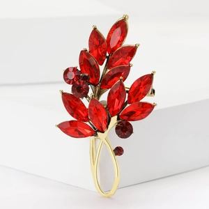 Vue détaillée d'une élégante broche feuille dorée aux cristaux rouges sur bloc blanc