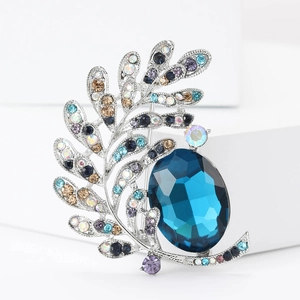 Detail view of rhinestone leaf brooch with large oval blue gemstone and silver metal