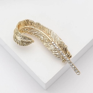 Elegant vintage gold feather brooch with sparkling white rhinestones on white pedestal