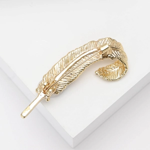 Detailed close-up of golden feather brooch with intricate metal textures on white stand