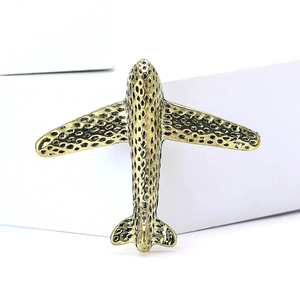 Retro golden airplane brooch with textured finish on minimalist white background