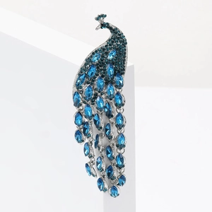 Broche paon élégante avec strass bleus et longue queue de cristal mobile sur fond blanc