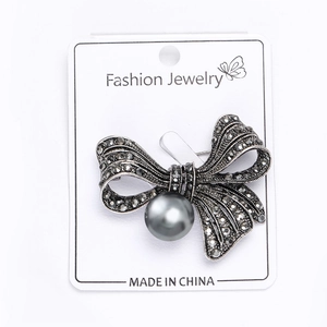 Detail of vintage bow brooch with grey rhinestones and a large center pearl on display