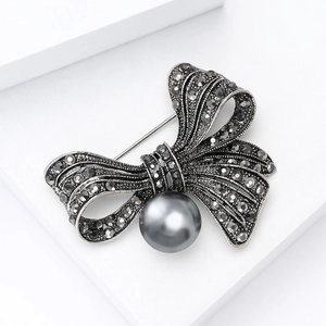 Vintage bowknot brooch with grey rhinestones and center pearl on white stand