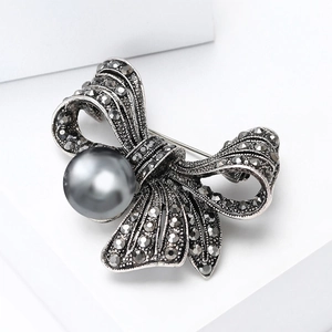 Detailed view of vintage bow brooch with grey rhinestones and large pearl on a white pedestal