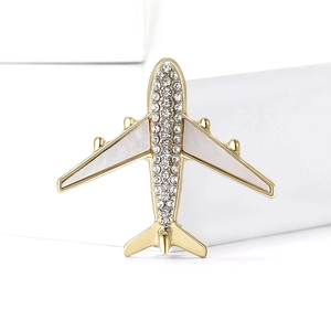 Elegant gold airplane brooch with white rhinestones on minimalist white block pedestal