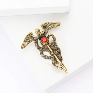 Broche caducée vintage dorée avec ailes d'ange et pierre rouge sur socle blanc