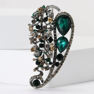 Vintage silver alloy leaf brooch with emerald crystals and rhinestones on white display