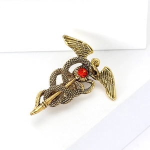 Broche caducée vintage dorée avec pierre rouge et ailes sur un support blanc