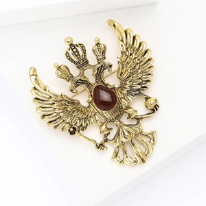Vintage gold double-headed eagle brooch with red gemstone on a white pedestal