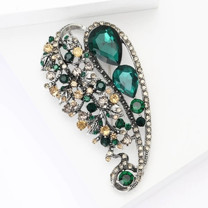 Vintage silver alloy leaf brooch with emerald crystals and rhinestones on white steps