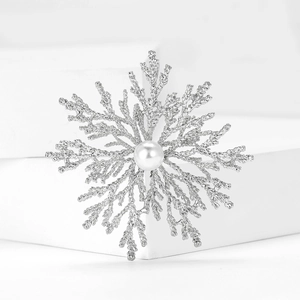Macro detail of silver snowflake brooch featuring matte texture and a central white pearl