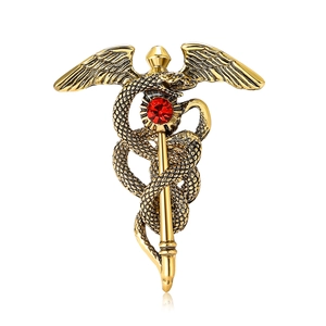 Broche ailes de caducée en or antique ornée d'un strass rouge au centre