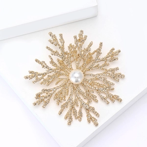 Golden snowflake brooch with central white pearl on a minimalist white display