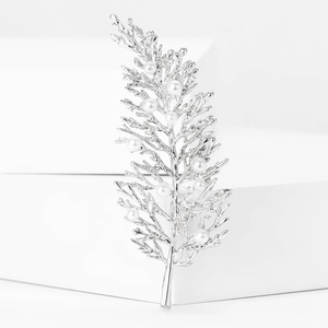 Elegant silver leaf brooch with white pearls on a minimalist white display base