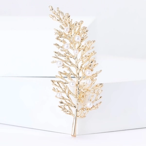 Elegant gold leaf brooch with white pearls displayed on a minimalist white platform