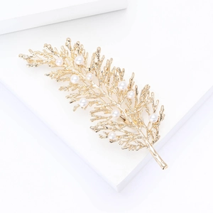 Detailed close-up of golden leaf brooch with elegant white pearls on a display block
