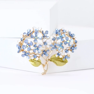 Detailed macro view of enamel hydrangea brooch with blue crystals on white geometric props