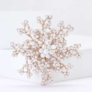 Elegant snowflake alloy brooch with white pearls and gold base on a white block