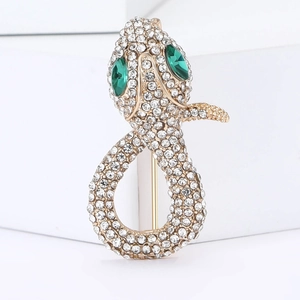 Macro view of gold snake brooch with white rhinestones and sparkling green gemstone eyes
