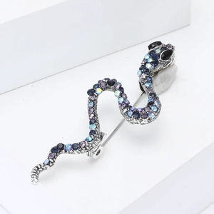 Broche serpent argentée avec strass colorés sur une plateforme géométrique blanche