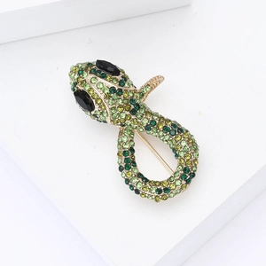 Macro detail of gold snake brooch with vibrant green rhinestones on stone background