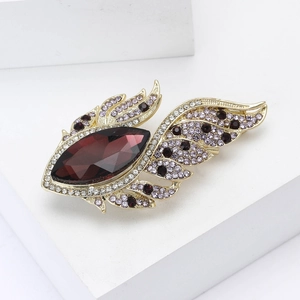 Elegant gold wing brooch with deep red marquise crystal and rhinestones on white background