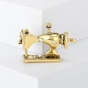 Vintage gold sewing machine brooch with sparkling rhinestones on a white podium