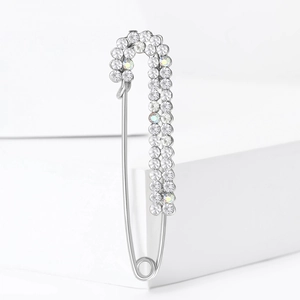 Elegant silver safety pin brooch with sparkling crystals on white minimalist pedestals