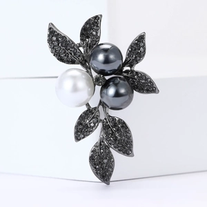 Vintage alloy leaf brooch with grey rhinestones and pearls on a white podium