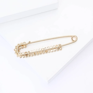 Close-up of golden alloy safety pin brooch with decorative scalloped edges on white blocks