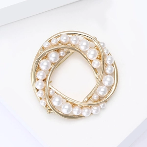 Broche couronne en perles et alliage doré pour costume femme sur un socle d'exposition