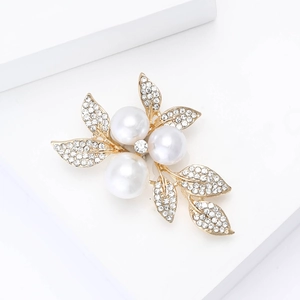 Detailed view of a gold leaf brooch with white pearls and sparkling crystal rhinestones